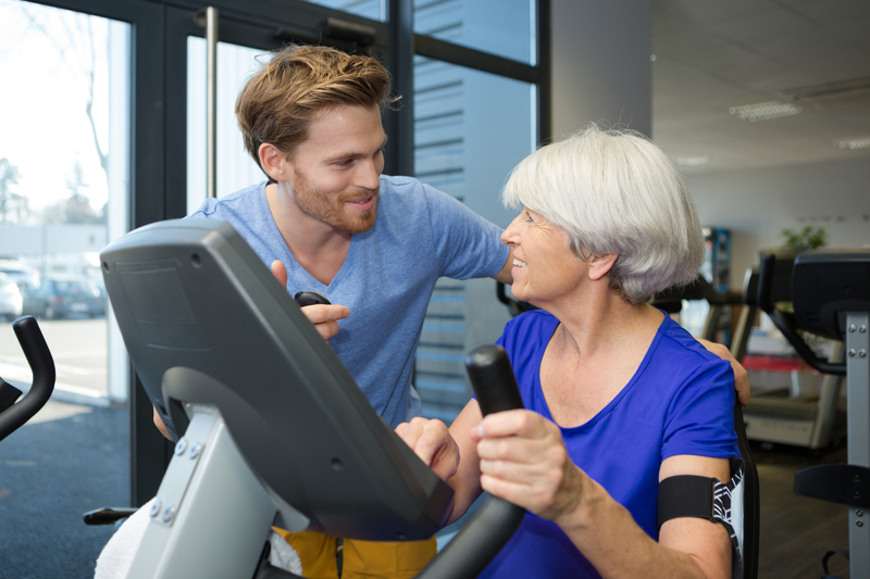 Older woman patient talking with a chiropractic and physical therapist as she is on an exercise machine